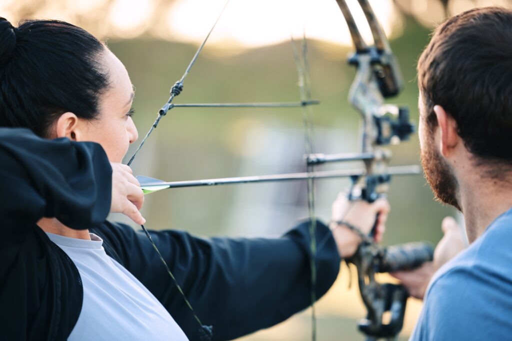 Archery, woman and target training with an instructor on a field for hobby, aim and control. Arrow,